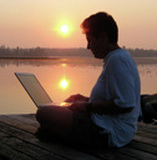 Photo of Helen sitting on dock typing on computer